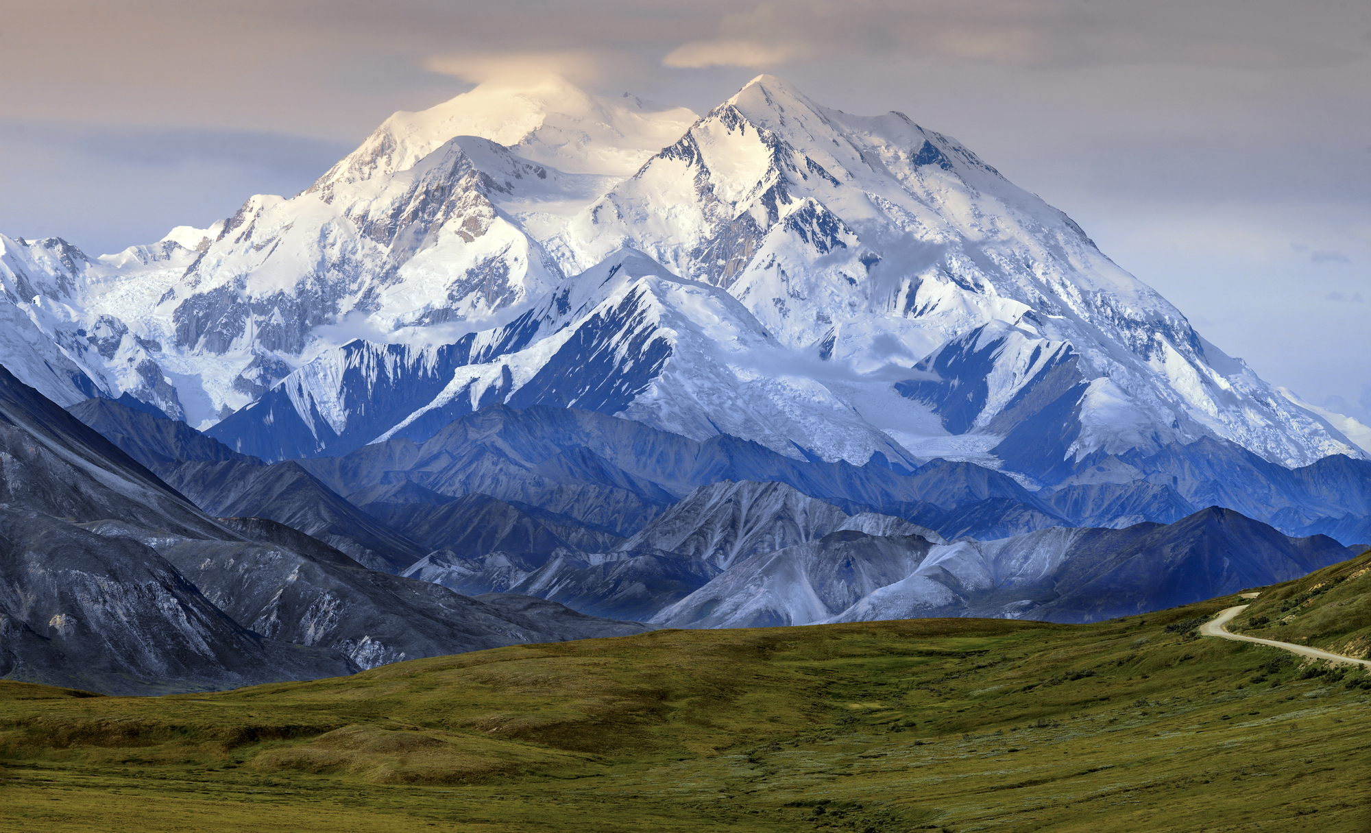 Denali mountain with snow-capped peak, rolling green tundra hills and winding road